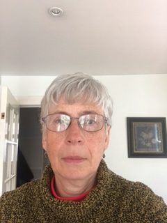 A photograph of Helen. She has glasses and a black and gold patterned sweater.