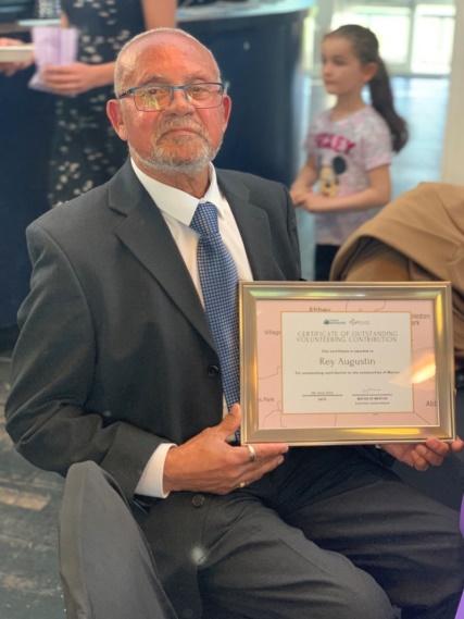 Volunteer Rey, dressed smartly in a grey suit and a blue tie, proudly displays his award.